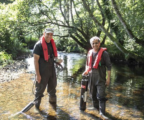 two men standing in a river holding scientific equipment